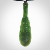 This is a sleek and slender hand carved New Zealand Jade mere pendant. The stone is a very dark green with mottled pale inclusions. The cord is black and adjustable. The pendant has a light polish and just glows. Hand carved by Kerry Thompson. One only pendant.